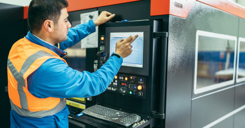 Worker operating a CNC machine control panel on a factory floor